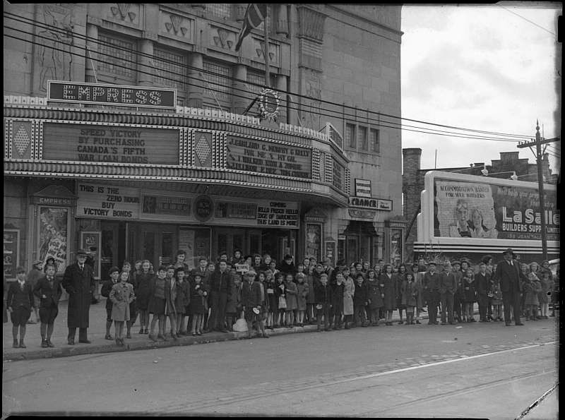 Empress Theatre en 1943. Groupe d'écoliers à la sortie du Empress Theatre situé au 5560, rue Sherbrooke Ouest à Montréal. L'enseigne lumineuse du cinéma encourage l'achat d'obligations de la Victoire et annonce le film For me and my Gal. Photo : Conrad Poirier, BanQ